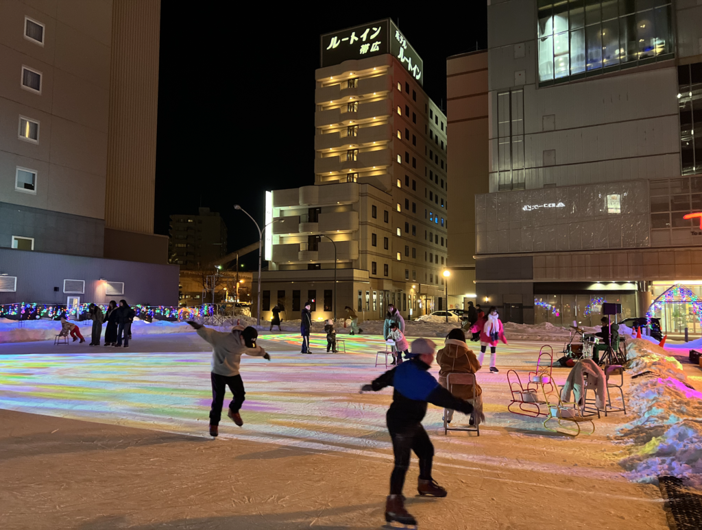 Visitors skating at Tokachi Ice Park Plus at night in front of Obihiro Station
